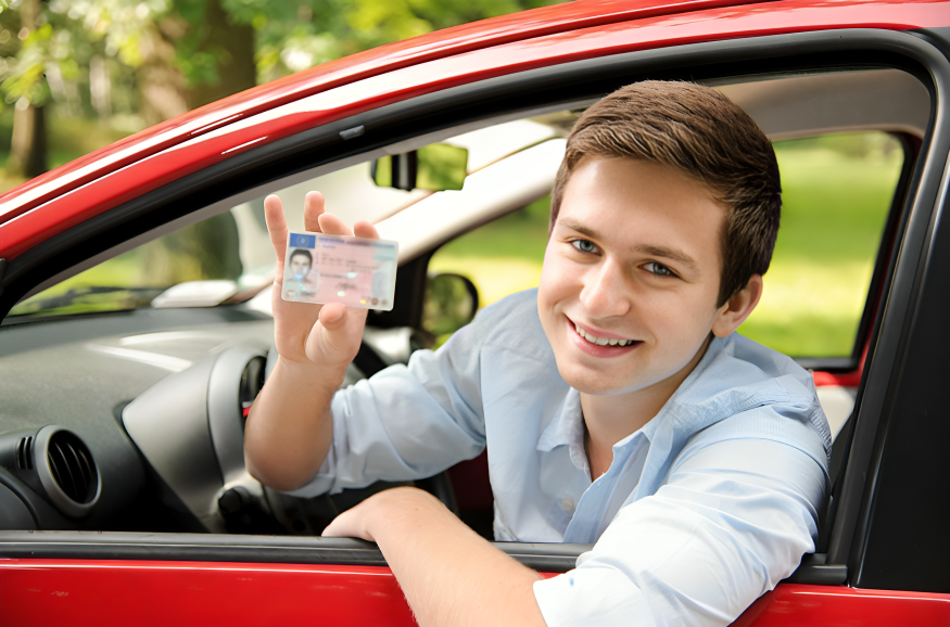 Smiling young man sitting in a red car holding an international driving licence, ready to take driving lessons in Milton Keynes with Trudo Driving Academy.